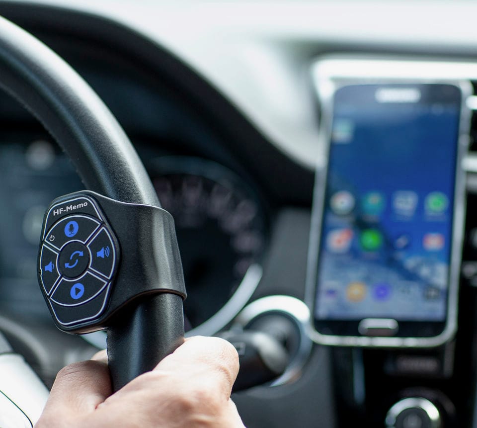 The HF-Memo remote on a steering wheel, with an Android phone on the dashboard