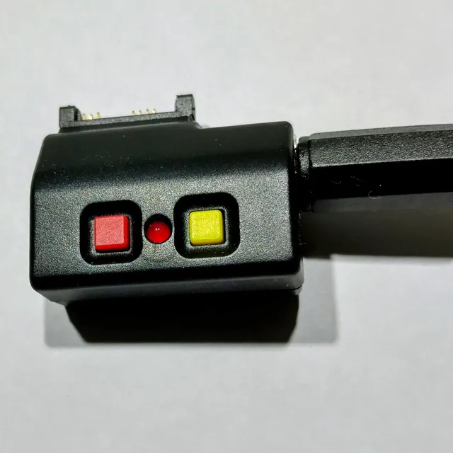 A small black headset adapter with a red and a yellow button and an LED